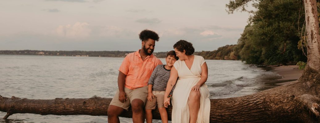 A joyful family enjoying quality time sitting on a log by the seaside during sunset.